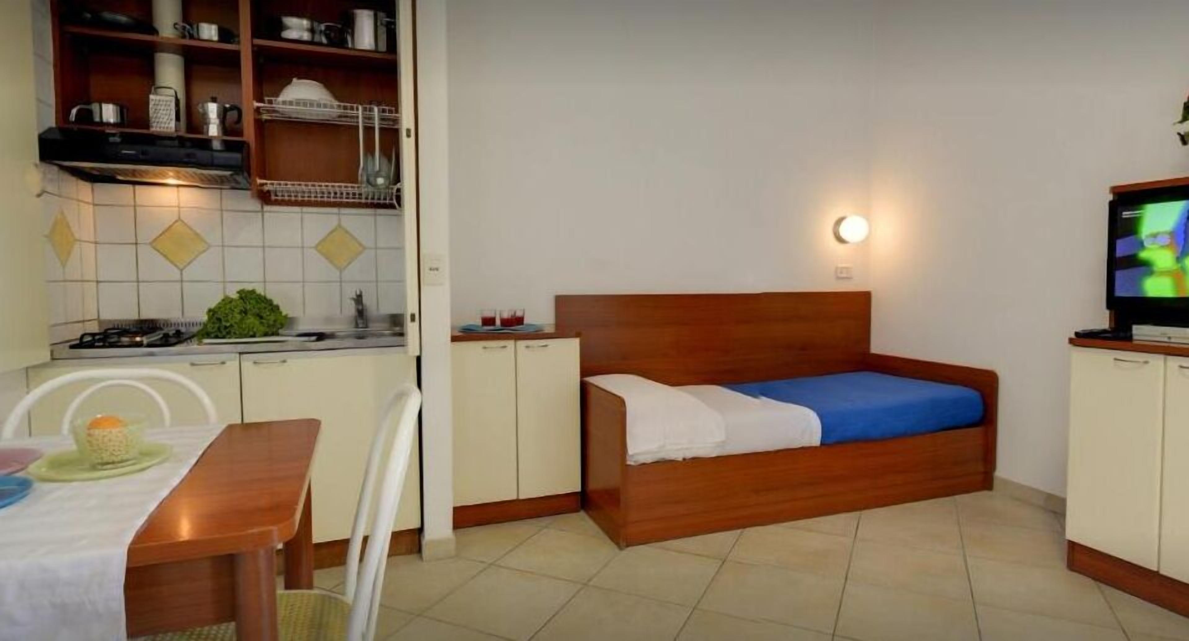 A compact room with a bed, a dining table, and a kitchenette.