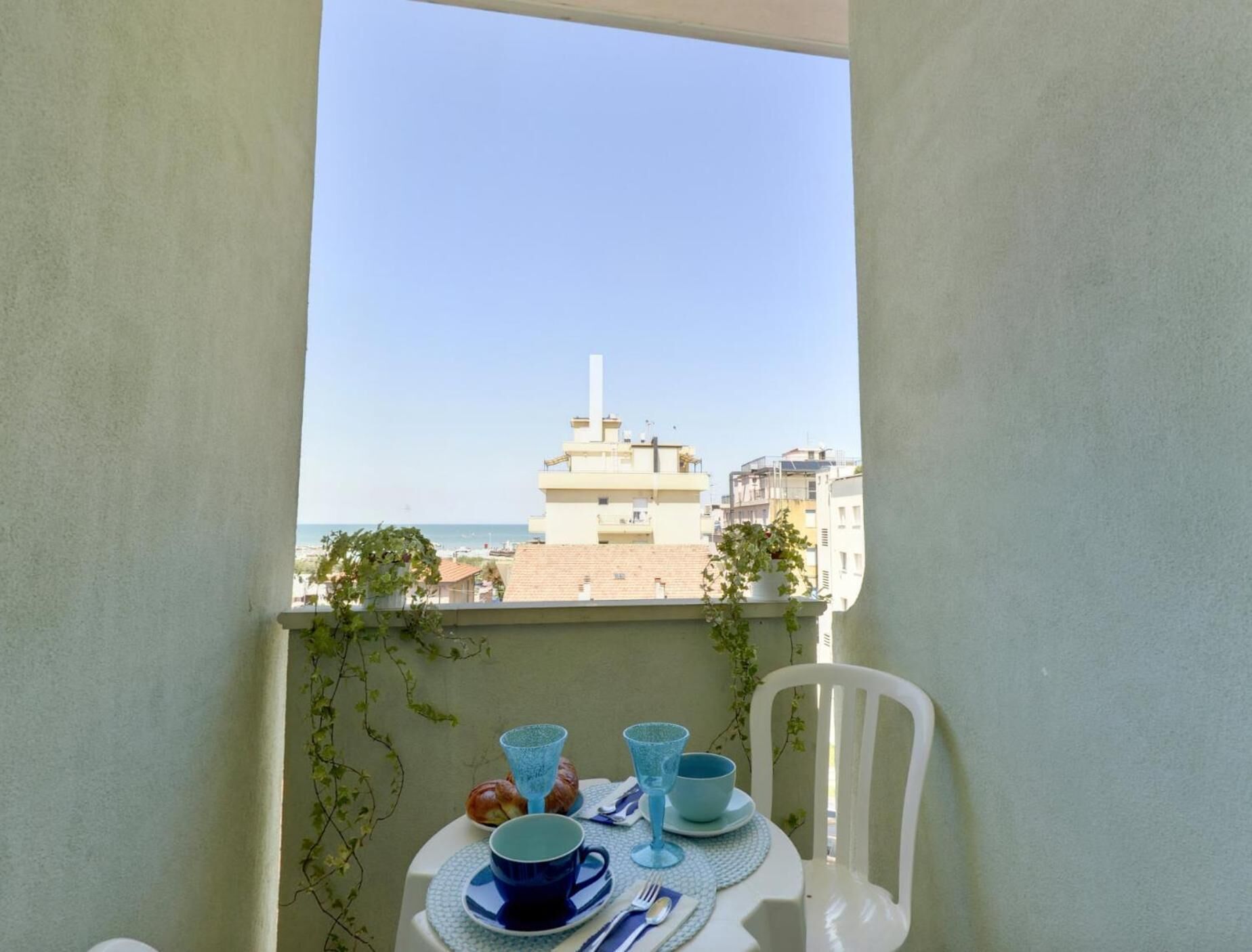 Ein Balkon mit Tisch für zwei Personen, mit Blick auf eine Stadtlandschaft und ein Gebäude mit einem hohen Schornstein.