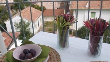 En balkon med et bord dækket til et måltid, med udsigt over et kystområde med bygninger og en klar himmel.