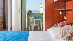 A hotel room with a bed, a small balcony with a table and chairs, and a view of the sea.