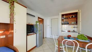 Une cuisine compacte équipée d’un réfrigérateur, d’une cuisinière et de placards. On y trouve une table à manger avec des chaises, ainsi qu’une petite plante accrochée au mur.