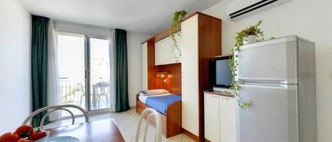 A compact hotel room with a kitchenette, a bed, a dining area, and a balcony.