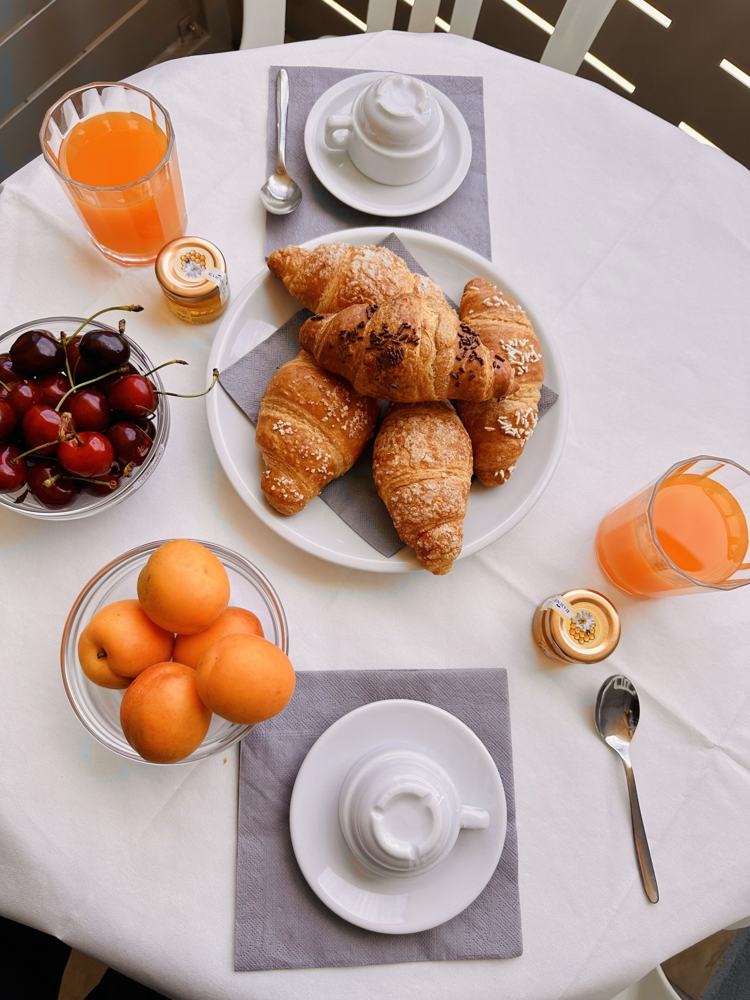 Ein Esstisch mit Croissants, Kirschen, Orangen, einem Teekessel und einer Kanne Orangensaft.