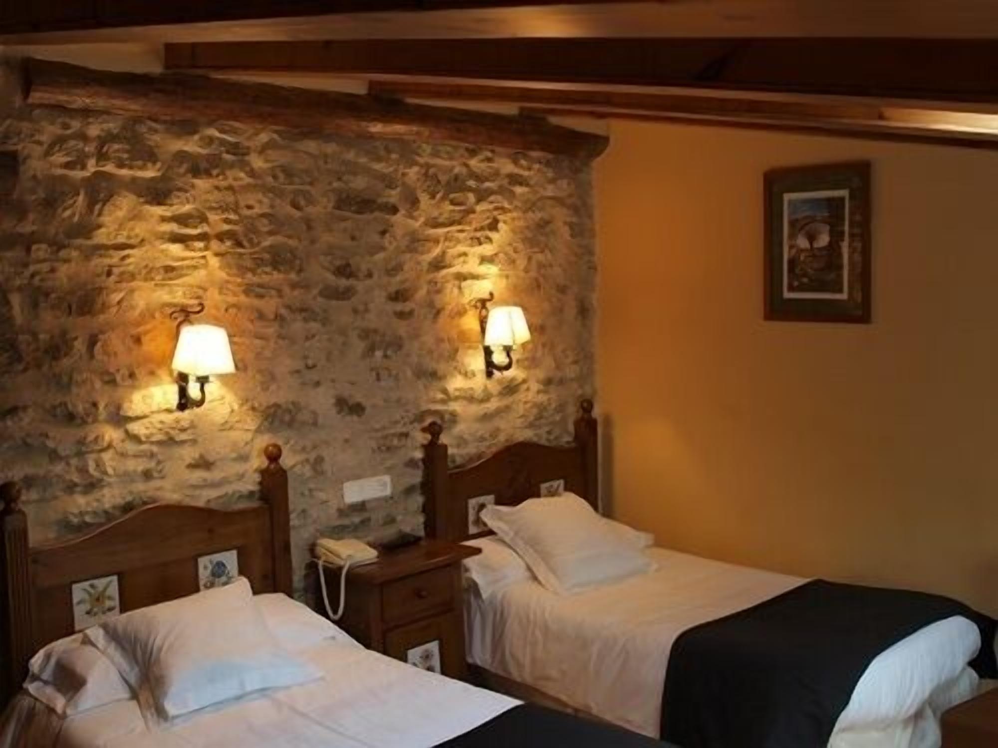 Una habitación con dos camas, paredes de piedra y lámparas fijadas a la pared.