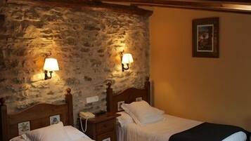 Una habitación con dos camas, paredes de piedra y lámparas fijadas a la pared.