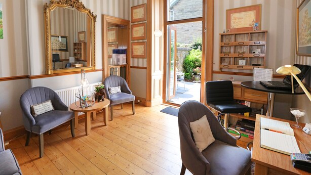 A room with striped wallpaper, a large mirror, two armchairs, a wooden desk with a laptop, and a bookshelf. - Lauderville Guest House (Edinburgh)