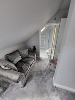 A small, dimly lit attic room with a worn-out sofa, a small table with a kettle, and a chair.