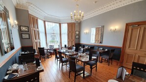 A dining area with wooden floors, tables set with plates, glasses, and cutlery. There are chairs around the tables, and a chandelier hangs from the ceiling. - Lauderville Guest House (Edinburgh)