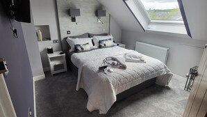 A bedroom with a sloped ceiling, a skylight, a bed with a white duvet, a bedside table, a wall-mounted TV, and a radiator. - Lauderville Guest House (Edinburgh)
