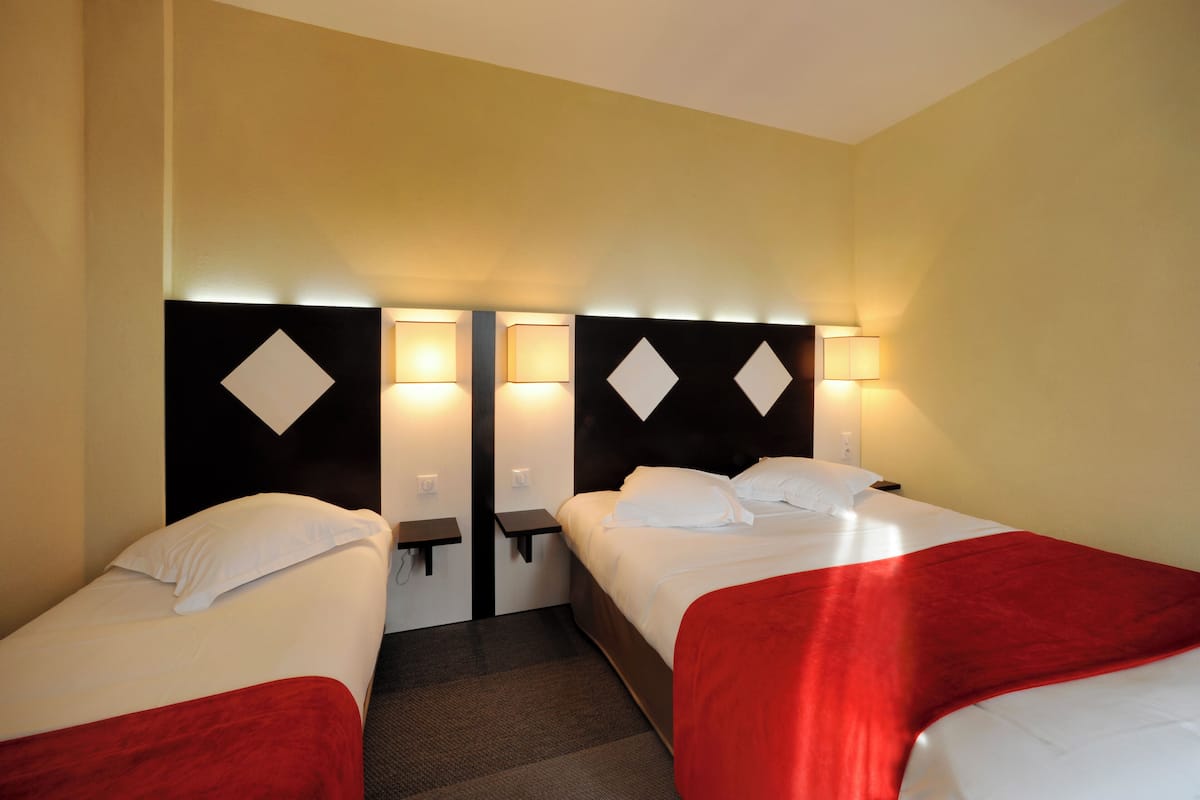 A hotel room with two beds, each with a red blanket, and a headboard with a diamond pattern.