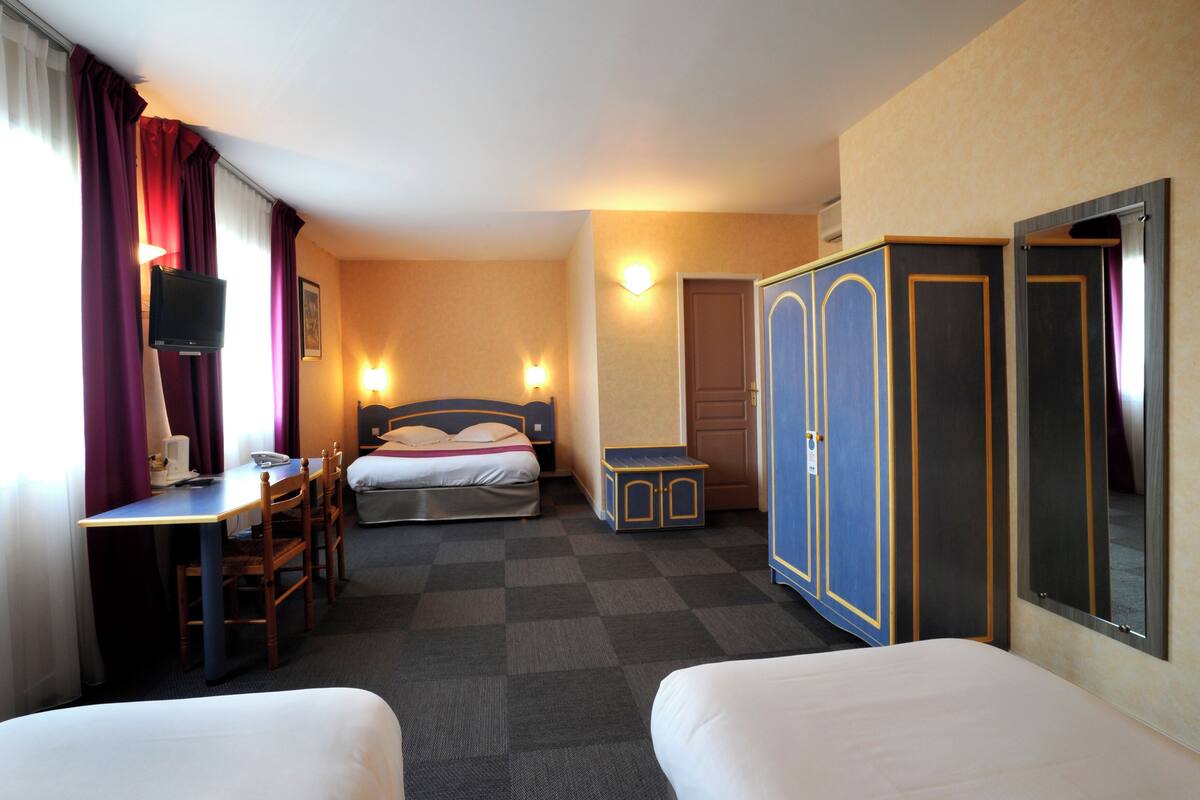 A hotel room with two single beds, a desk with a chair, a wardrobe, and a television.