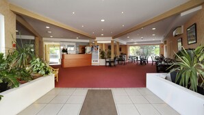 A hotel lobby with a reception desk, seating area, and potted plants. - The Originals City, Hôtel des Arènes, Saintes (Saintes)