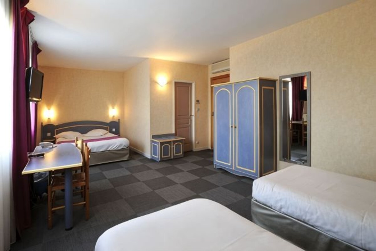 A hotel room with two beds, a desk, a chair, a wardrobe, and a mirror.