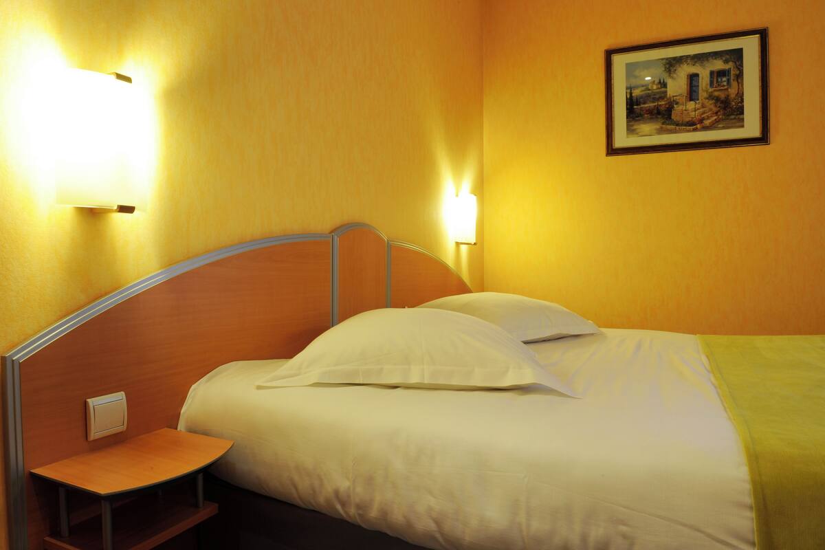 A hotel room with a bed, bedside table, and two wall-mounted lights.