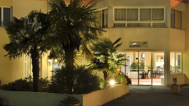 A hotel entrance with a reception desk, palm trees, and a parking sign. - The Originals City, Hôtel des Arènes, Saintes (Saintes)