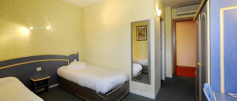 A hotel room with two beds, a desk, a wardrobe, and a mirror.