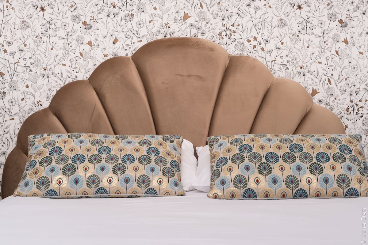 A bed with a tufted headboard and decorative pillows with a peacock feather pattern.