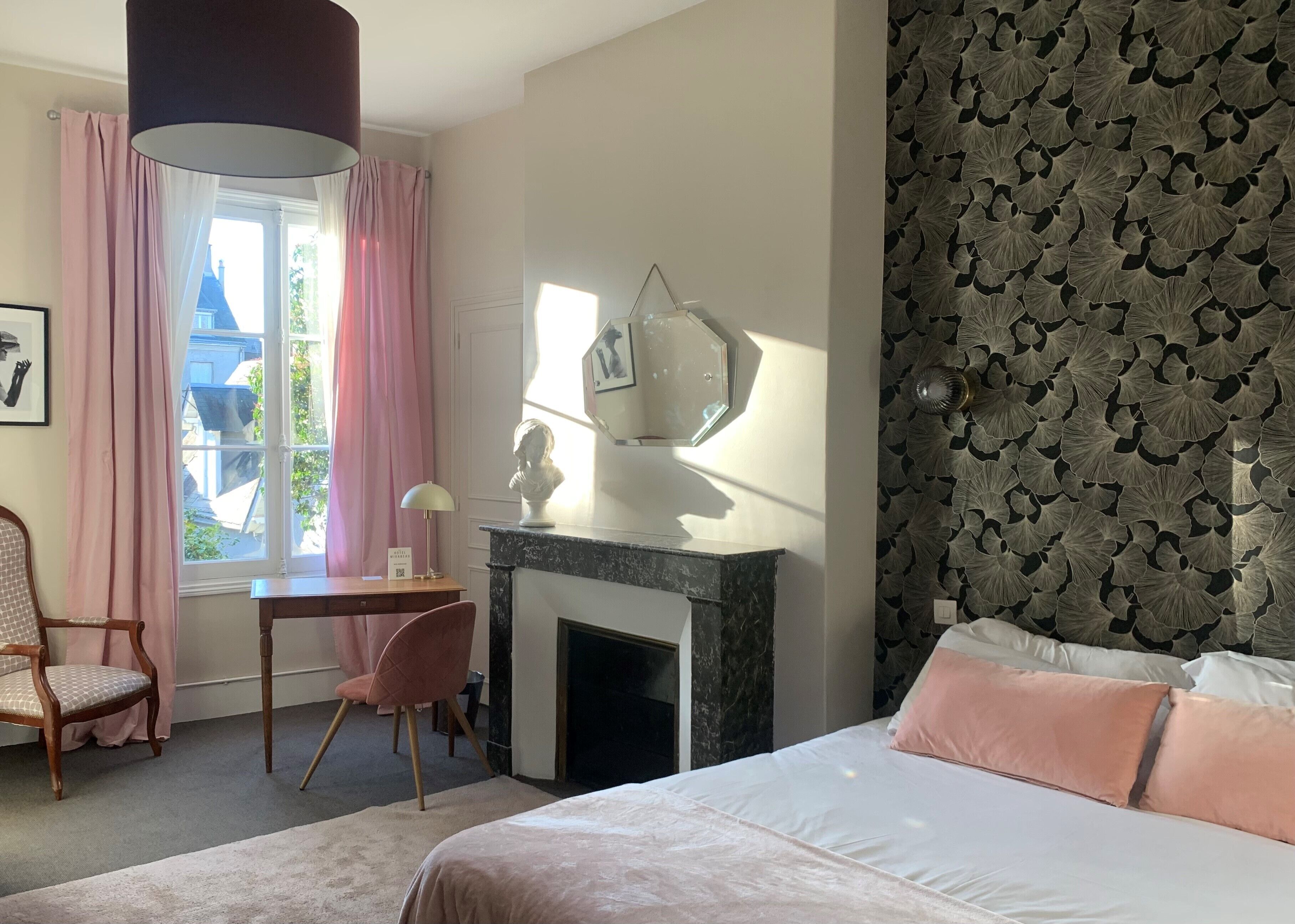 Un dormitorio con cama, escritorio, silla, chimenea y ventana con cortinas.