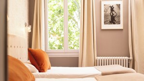 A bedroom with a bed, two pillows, a window with curtains, a radiator, and a framed picture on the wall. -  Hotel Mirabeau (Tours)