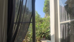 A window with sheer curtains, a view of a garden with various plants and a table with chairs outside. -  Hotel Mirabeau (Tours)