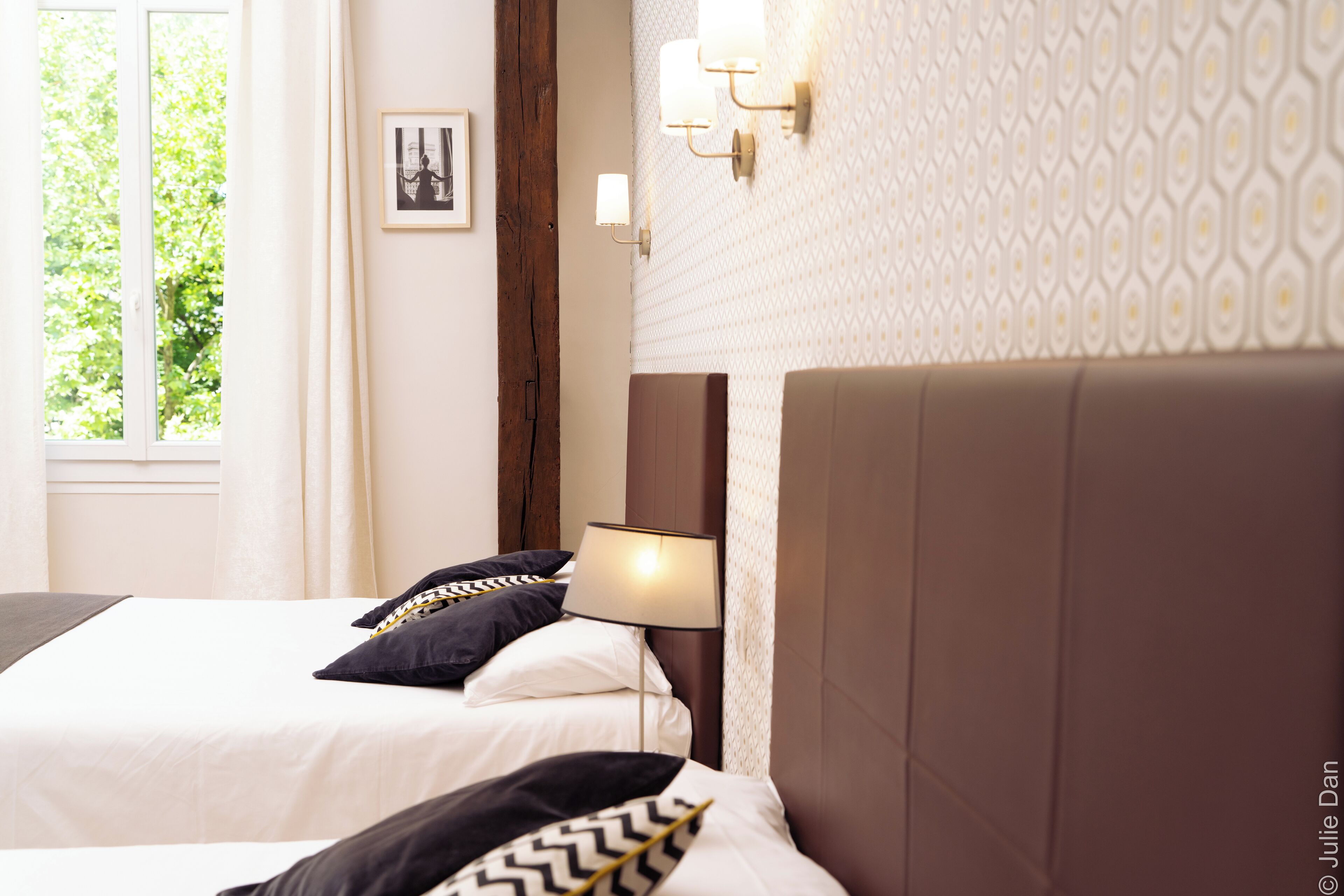 Une chambre d’hôtel avec deux lits, une fenêtre et un mur recouvert d’un papier peint à motifs.