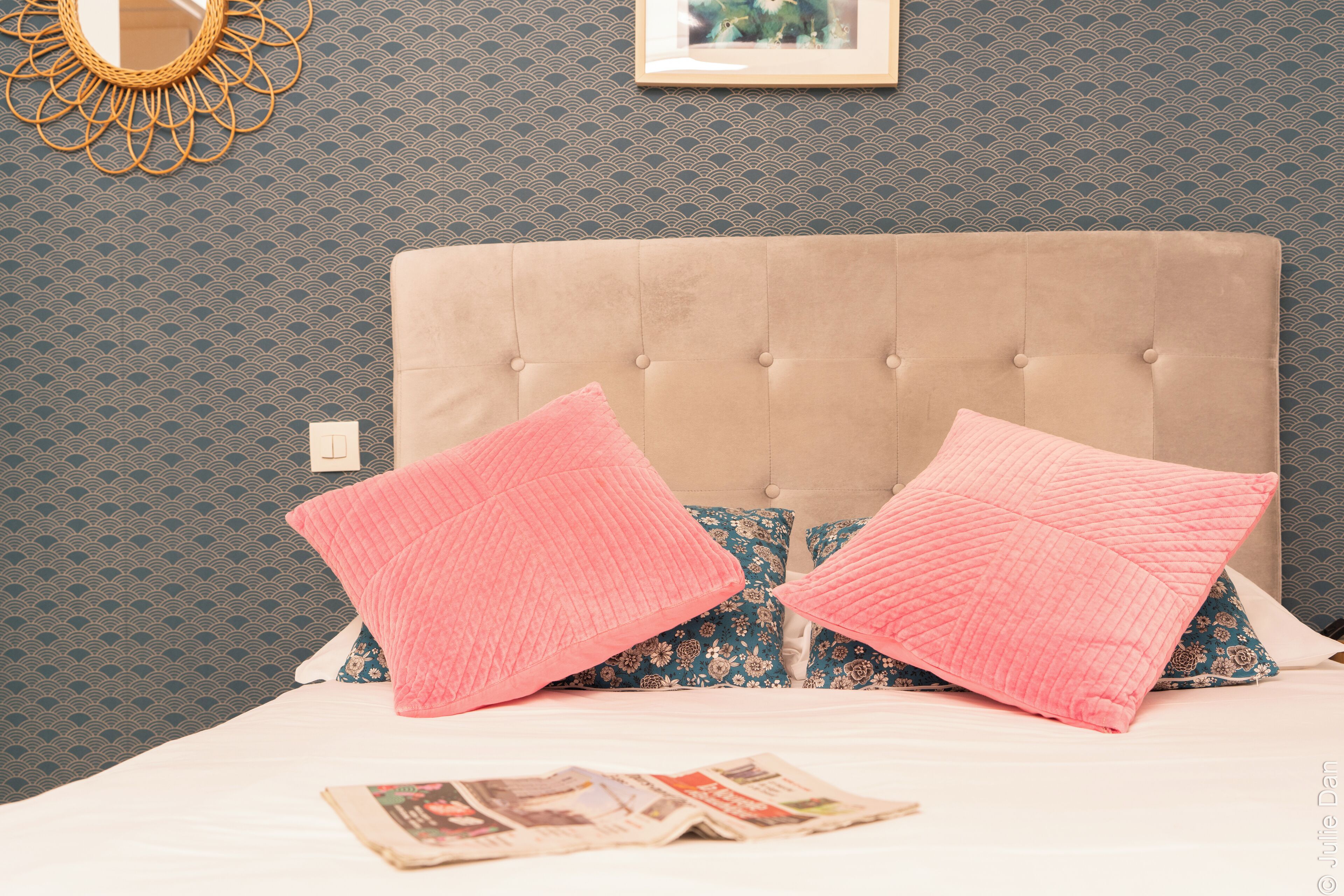 Ein Bett mit einer gebügelten Kopfteil, Kissen mit rosa und blauen Mustern und einem gerahmten Bild an der Wand.