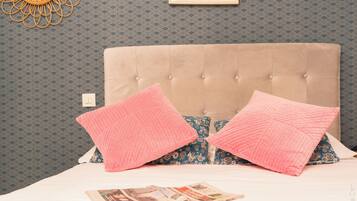 Ein Bett mit einer gebügelten Kopfteil, Kissen mit rosa und blauen Mustern und einem gerahmten Bild an der Wand.