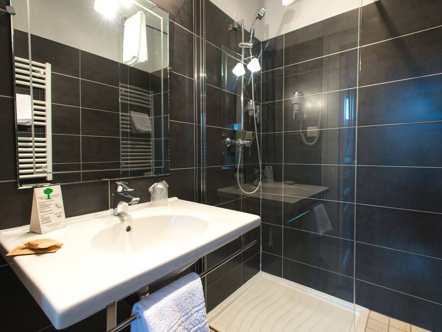 Un baño moderno con un lavamanos blanco, ducha con cerramiento de vidrio y paredes de azulejos oscuros.