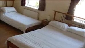 Two single beds with wooden frames in a room with a tiled floor. - Bennys B and B (London)