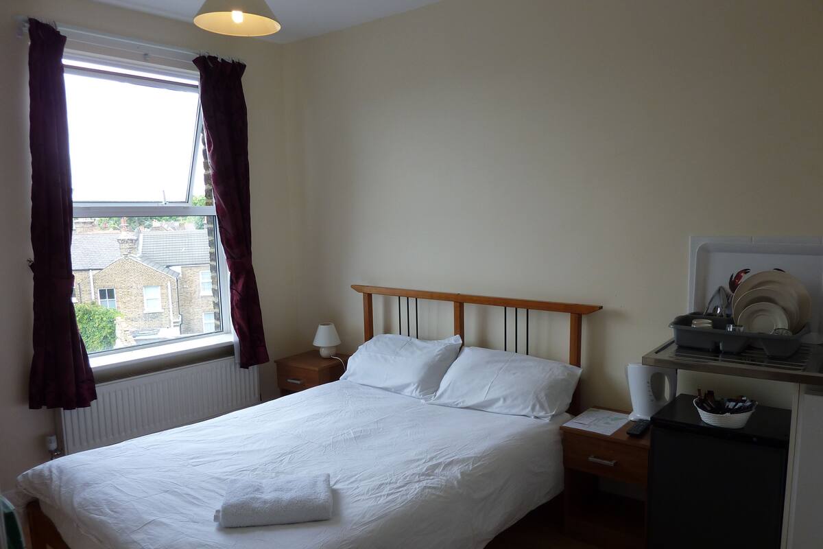 A neatly made bed with white linens, a bedside table with a lamp, and a small refrigerator.