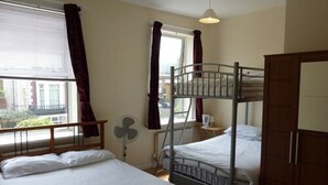 A room with bunk beds, a fan, a window with curtains, and a door. - Bennys B and B (London)