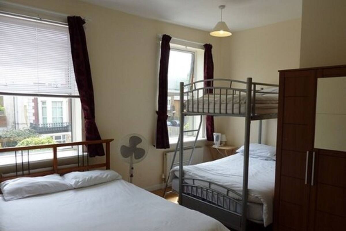 A room with bunk beds, a fan, a window with curtains, and a door.