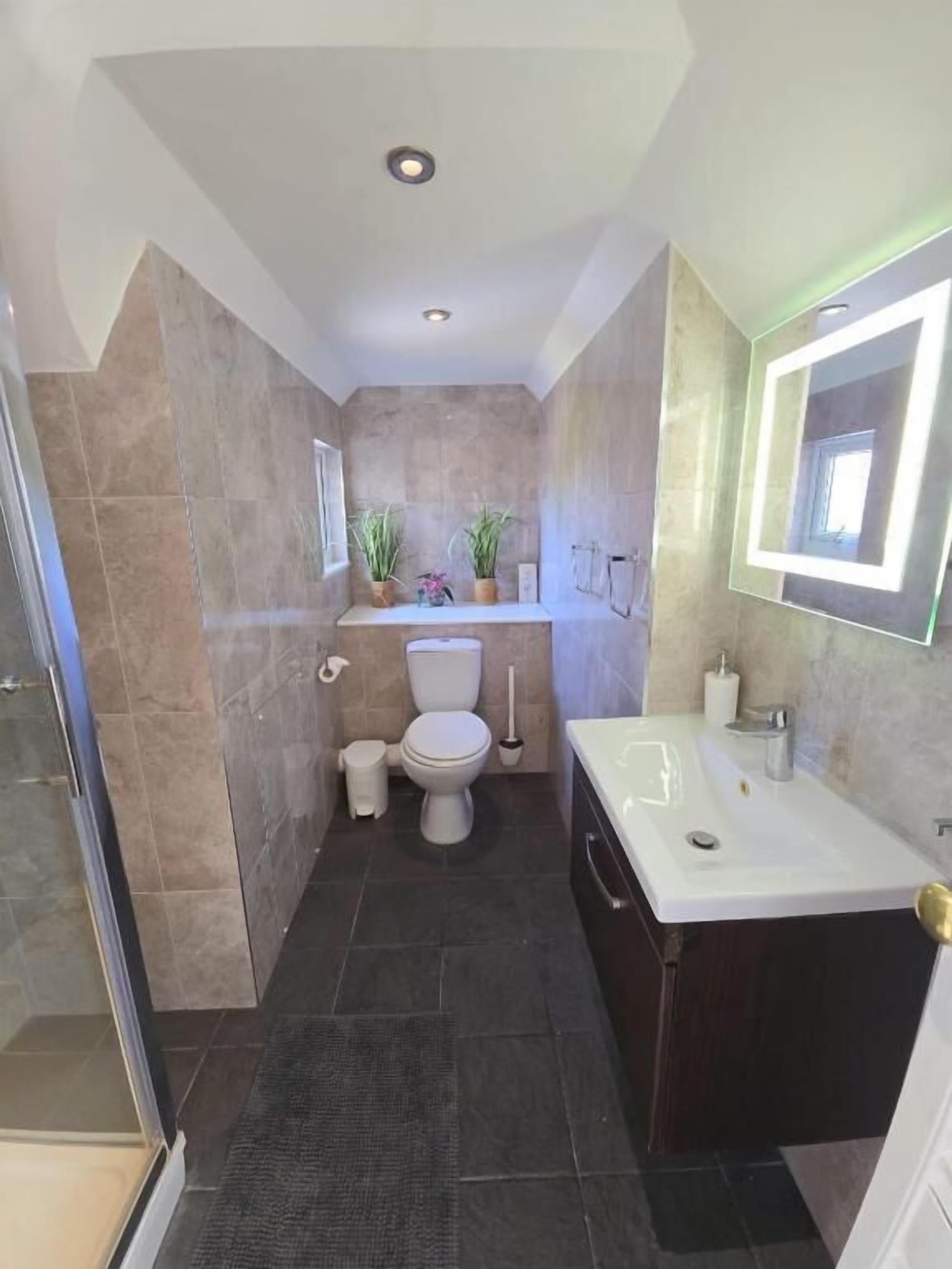 A modern bathroom with a shower, toilet, sink, and a mirror with LED lighting.