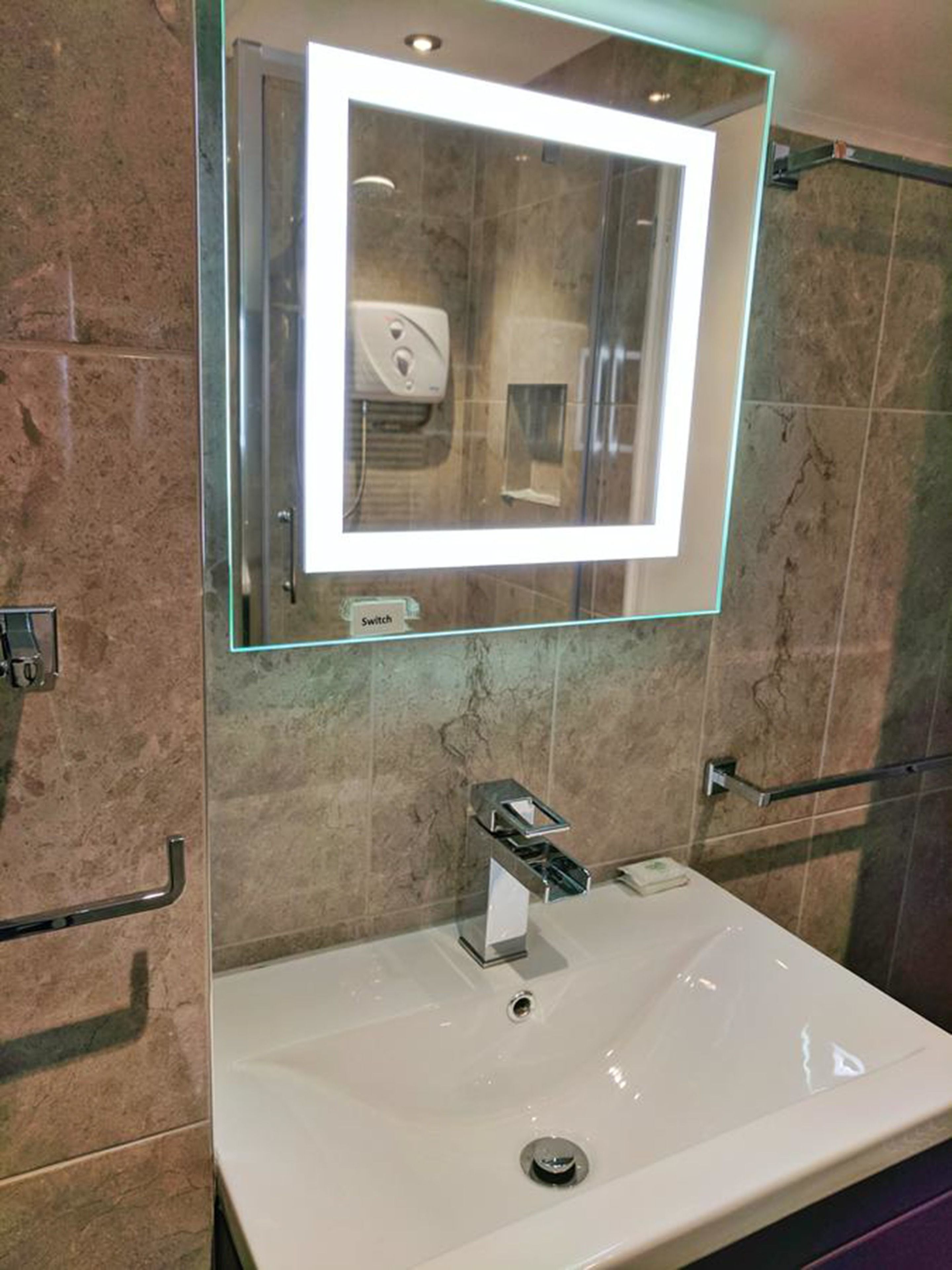 A bathroom with a glass-enclosed mirror, a sink, and a hand dryer.