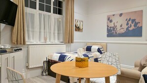 Un dormitorio acogedor con cama, mesita de noche, una mesa redonda de madera y una ventana con cortinas.