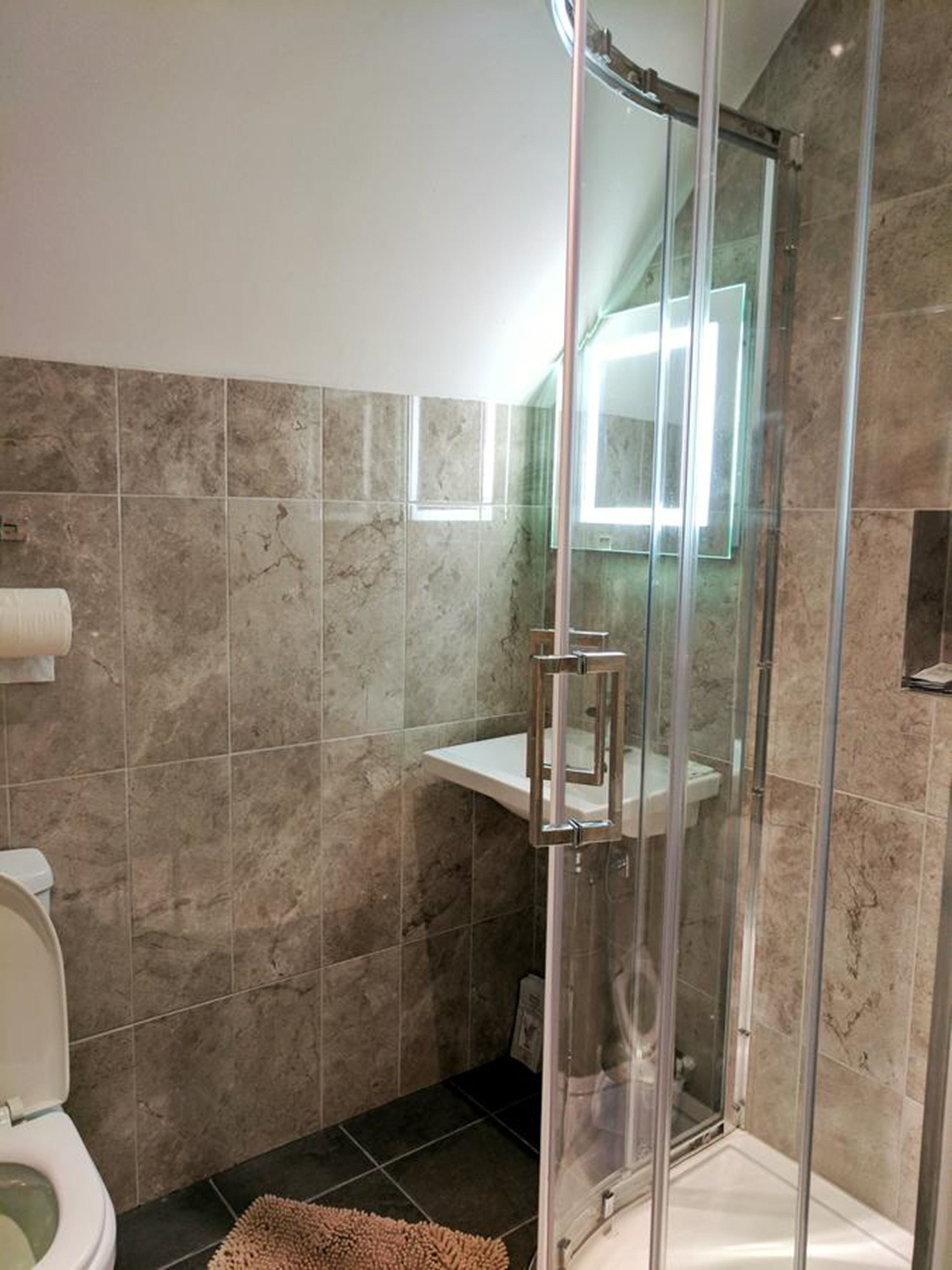 Un baño con ducha envuelta en vidrio, inodoro y lavabo con espejo.