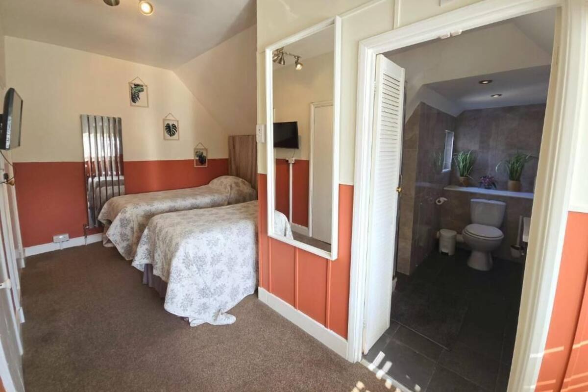 A room with two beds, a mirror, a television, and a bathroom visible through an open door.