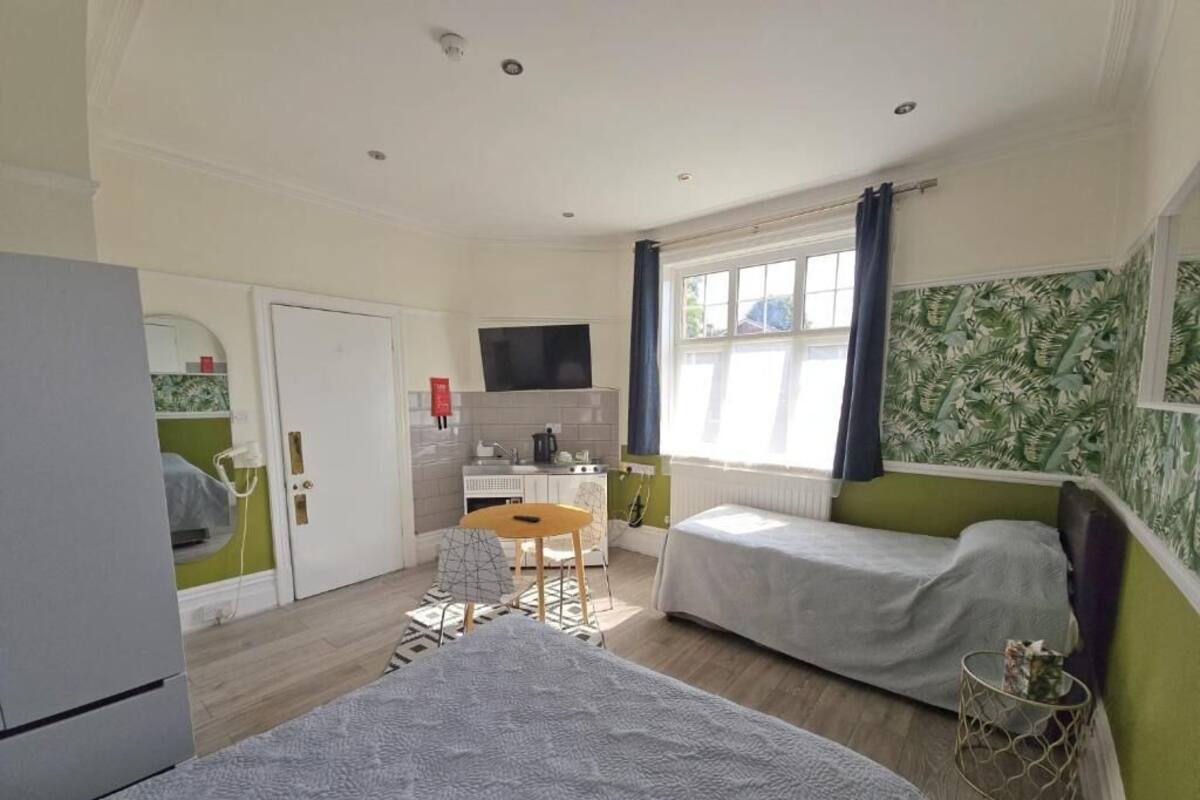 A compact room with two single beds, a small kitchenette, a dining area, and a TV.