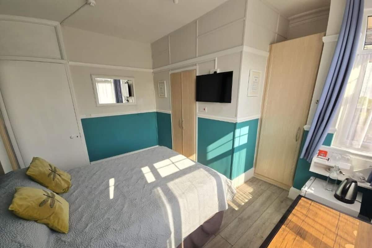 A hotel room with a bed, a TV, a wardrobe, and a small table with a kettle.