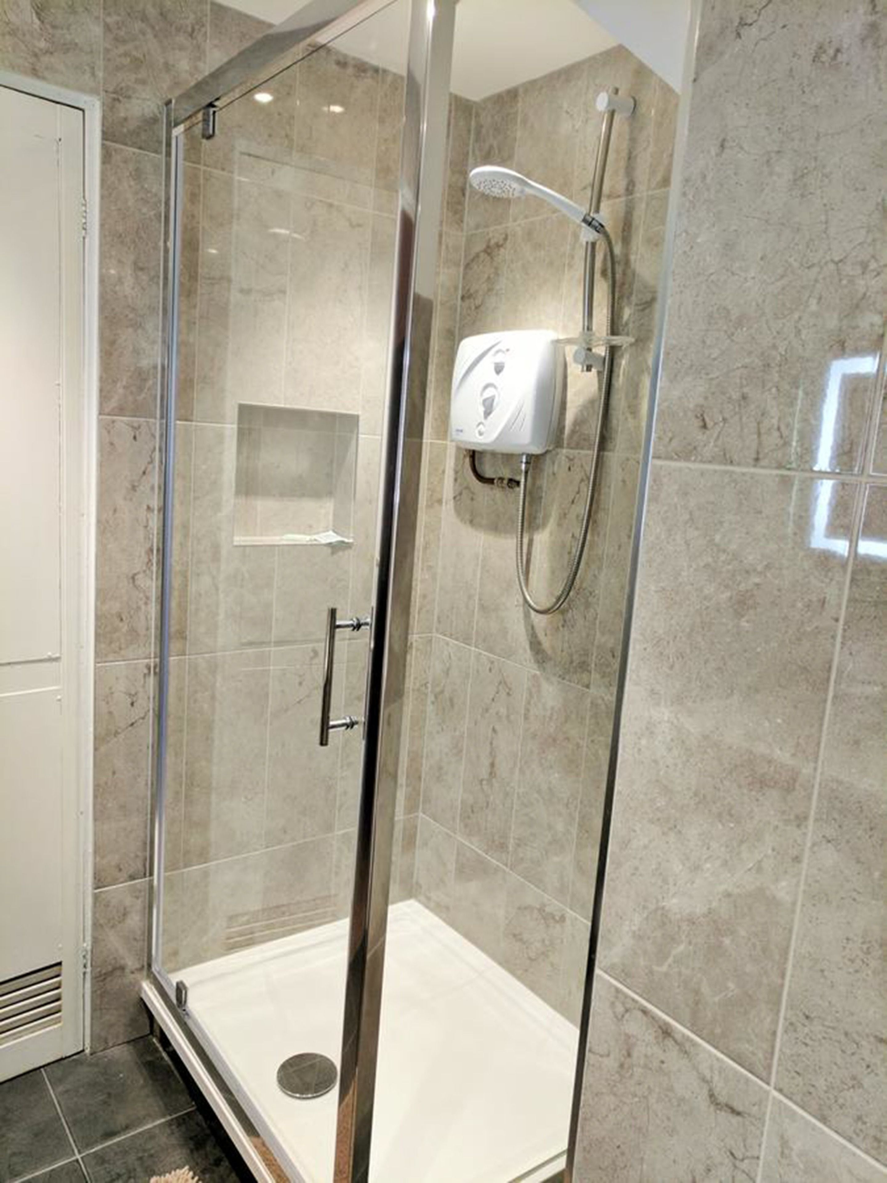 A glass-enclosed shower stall with a handheld showerhead and a wall-mounted control panel.