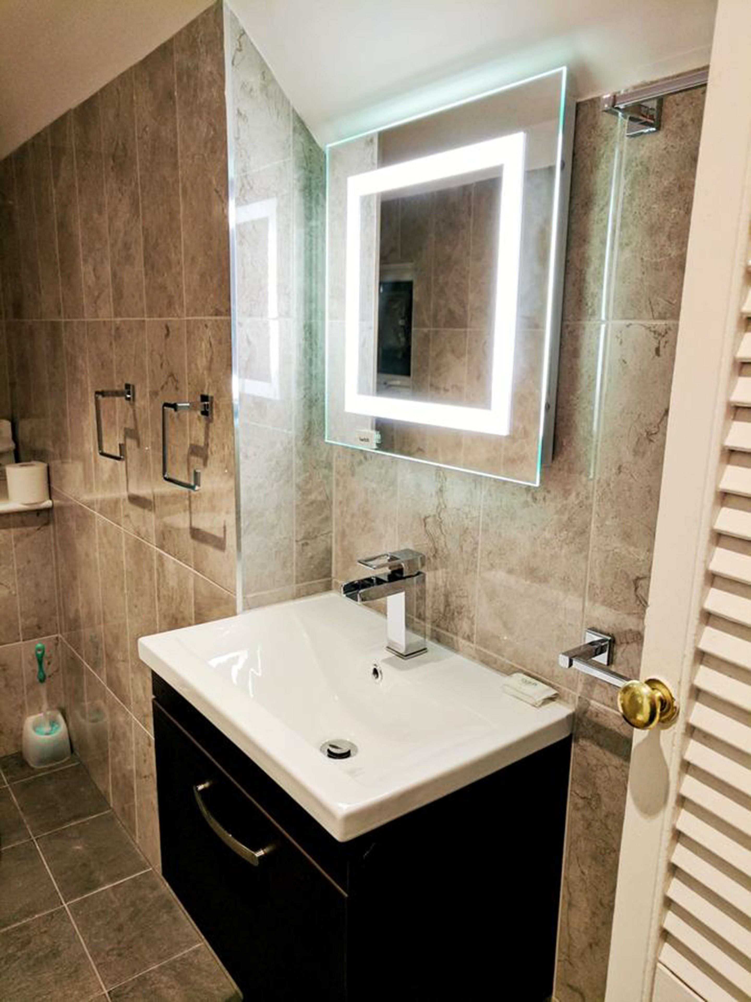 Un baño con un lavamanos blanco, un espejo con luz y una zona de ducha.