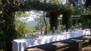 An outdoor dining area with a long table set for a meal, surrounded by greenery and a stone bench. - Kings Walden Garden Manor (Tzaneen)