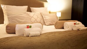 A neatly made bed with multiple pillows and rolled towels, a headboard, and a bedside lamp. - Kings Walden Garden Manor (Tzaneen)