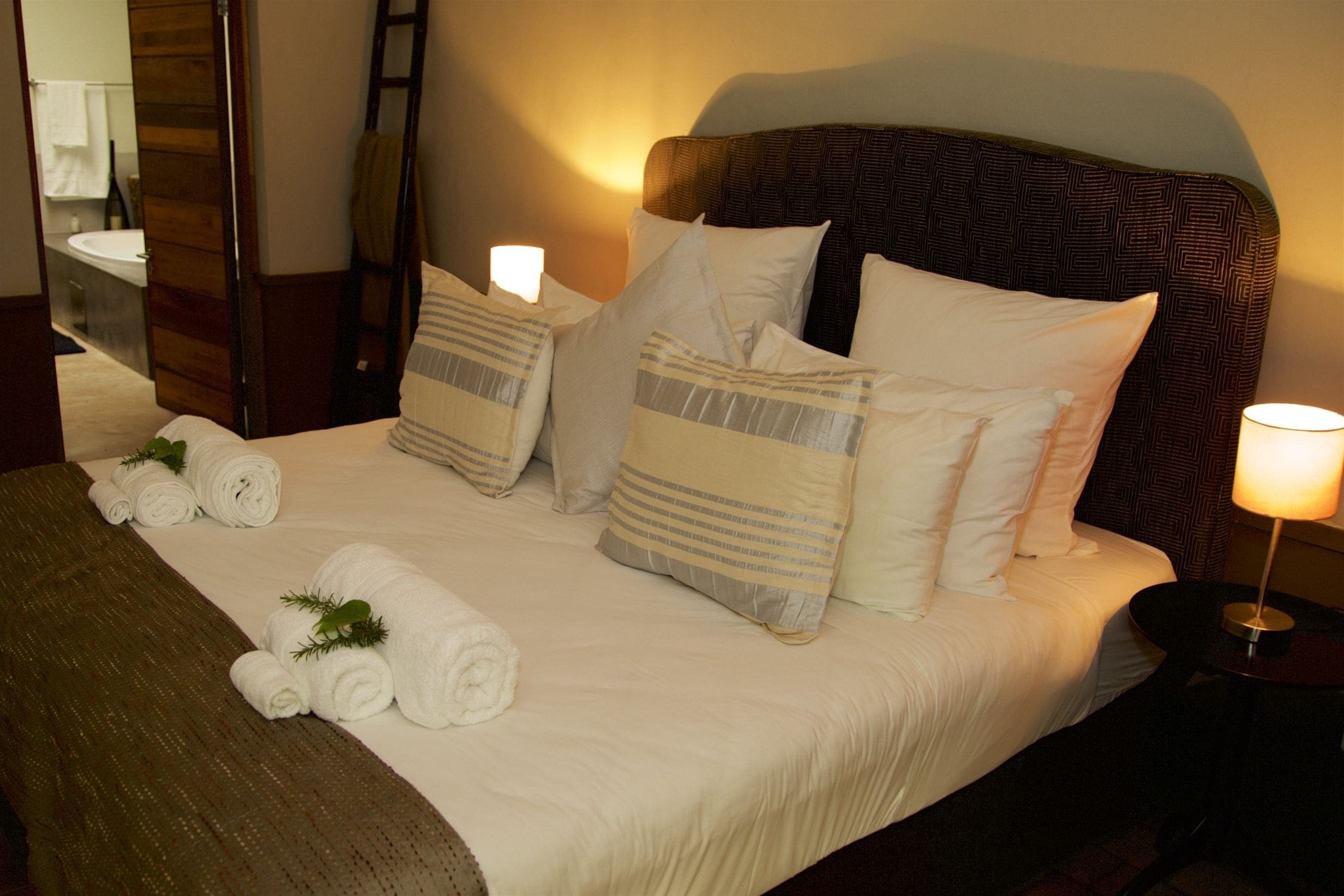 Una cama bien hecha con sábanas blancas, almohadas a rayas y toallas enrolladas.