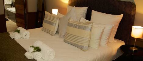 A neatly made bed with white linens, striped pillows, and rolled towels.