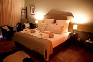 Een netjes ingerichte hotelkamer met een groot bed, twee nachtkastjes, een stoel en een kleine tafel met een lamp.