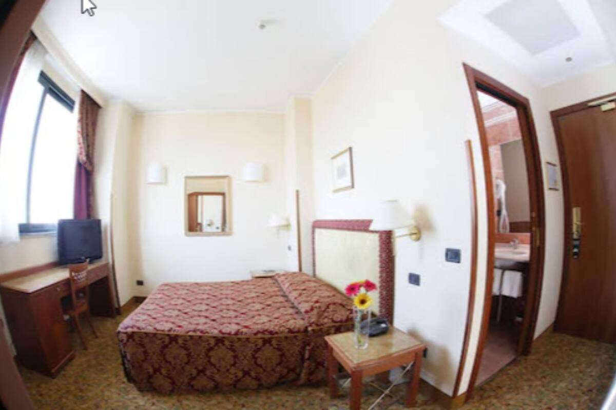 Ein Hotelzimmer mit Bett, Schreibtisch, Stuhl, Fernseher, Spiegel und einer Tür zum Badezimmer.