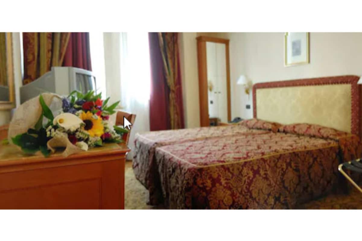 Ein Hotelzimmer mit einem Bett, einem Schreibtisch mit Blumen, einem Fernseher und einem Spiegel.