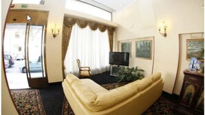 Ein Hotelzimmer mit einer Couch, einem Fernseher, einer Pflanze und Kunstwerken an den Wänden.