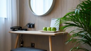 Un espacio de trabajo con un escritorio de madera, un taburete pequeño, un espejo redondo, un teléfono y una planta.